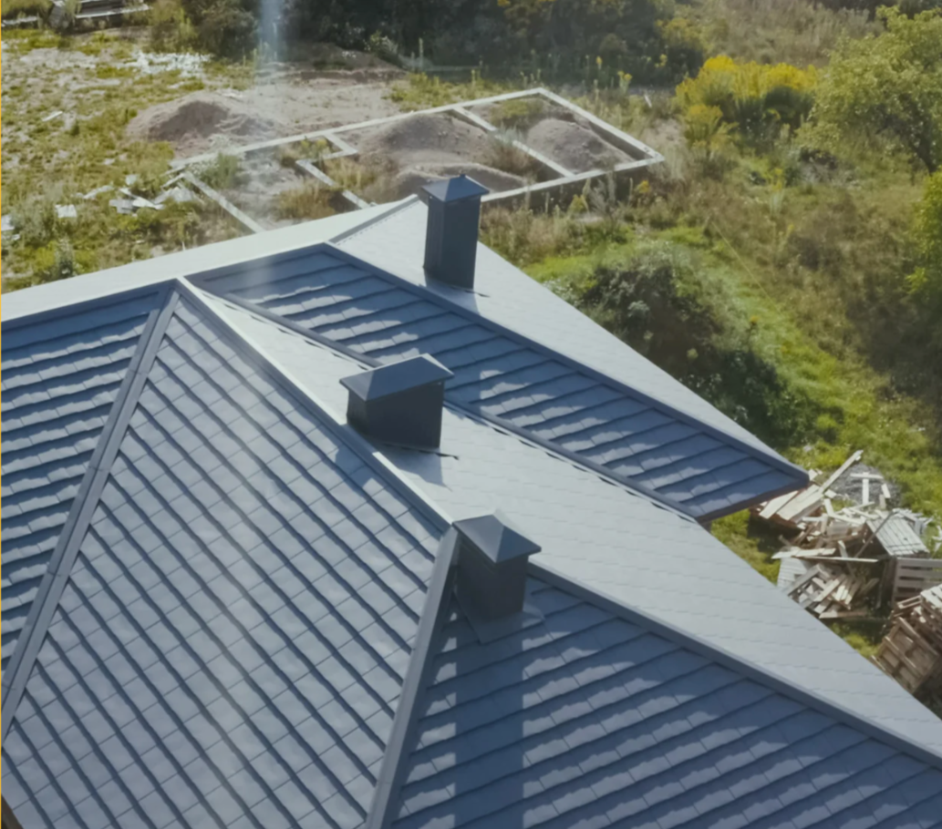 Modern blue roof with chimneys and greenery.